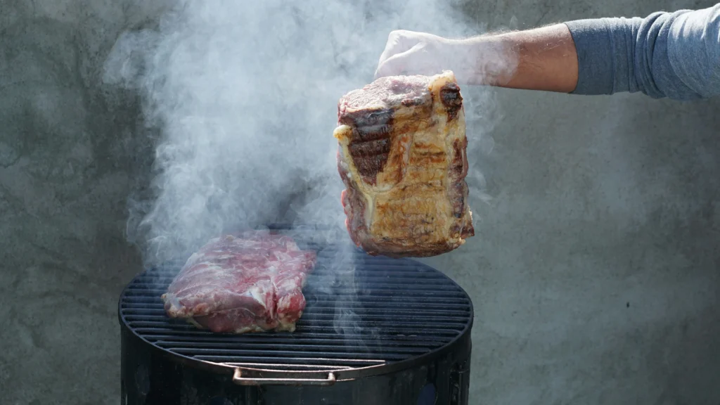 Man holding a piece of meat over a grill